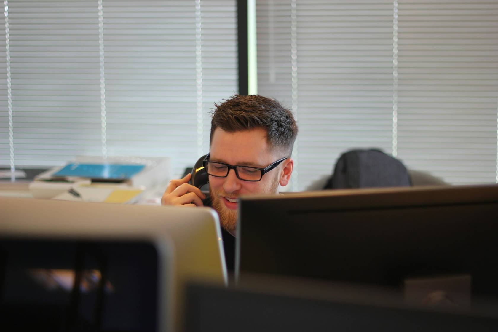 Person wearing eyeglasses using an electronic device near an office window with window blinds.